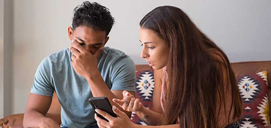 A woman shows a smartphone to a distressed man on a couch, possibly displaying contact information for Arlington Heights business law attorneys.