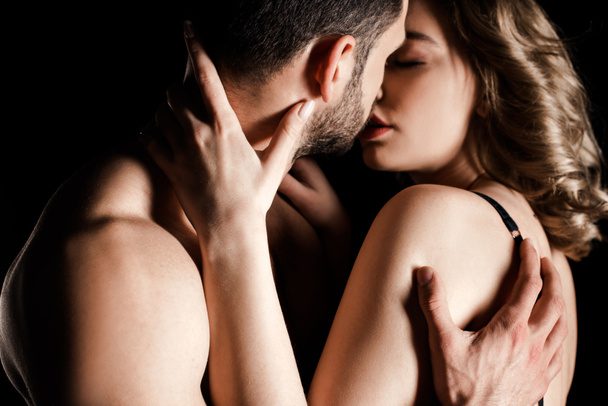 A shirtless man and a woman in a black bra are embracing closely and about to kiss, set against a dark background, capturing an intimate moment amidst the complexities life can bring—sometimes even needing the guidance of a Chicago divorce attorney.