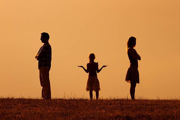Silhouette of a man and woman standing facing away from each other with a child in between them, arms outstretched, during sunset—a poignant moment that many Chicago divorce attorneys witness in their practice.